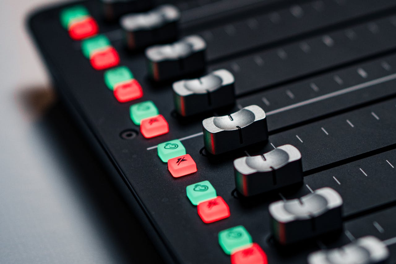 Close-up of an illuminated studio audio mixing console with colorful buttons and sliders.